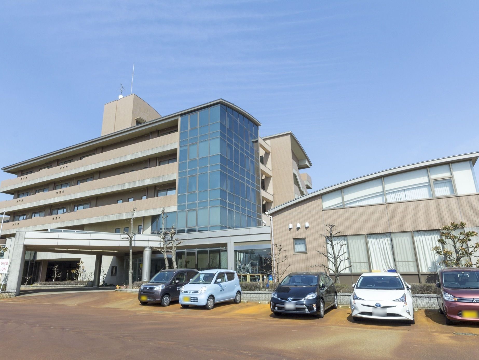 大きなタイル貼りの建物が建っている。建物全体に日差しが当たっている。玄関ポーチにコンクリート調のひさしがある。