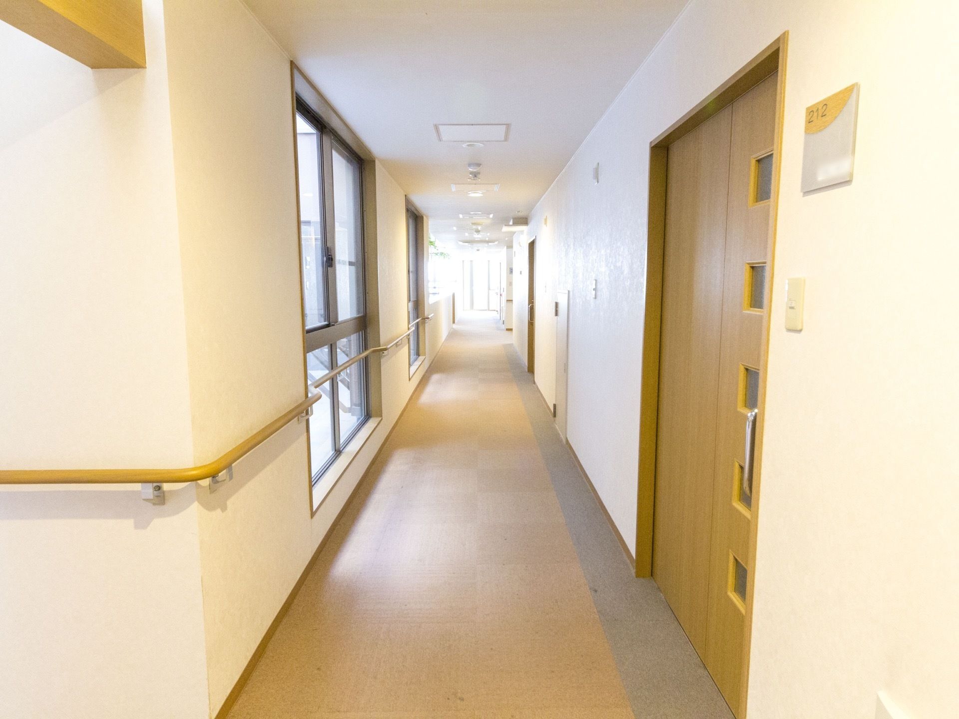 窓が設置されている。窓の前にも手すりが設置されている。木目調の居室の扉があり、部屋番号が貼られている。