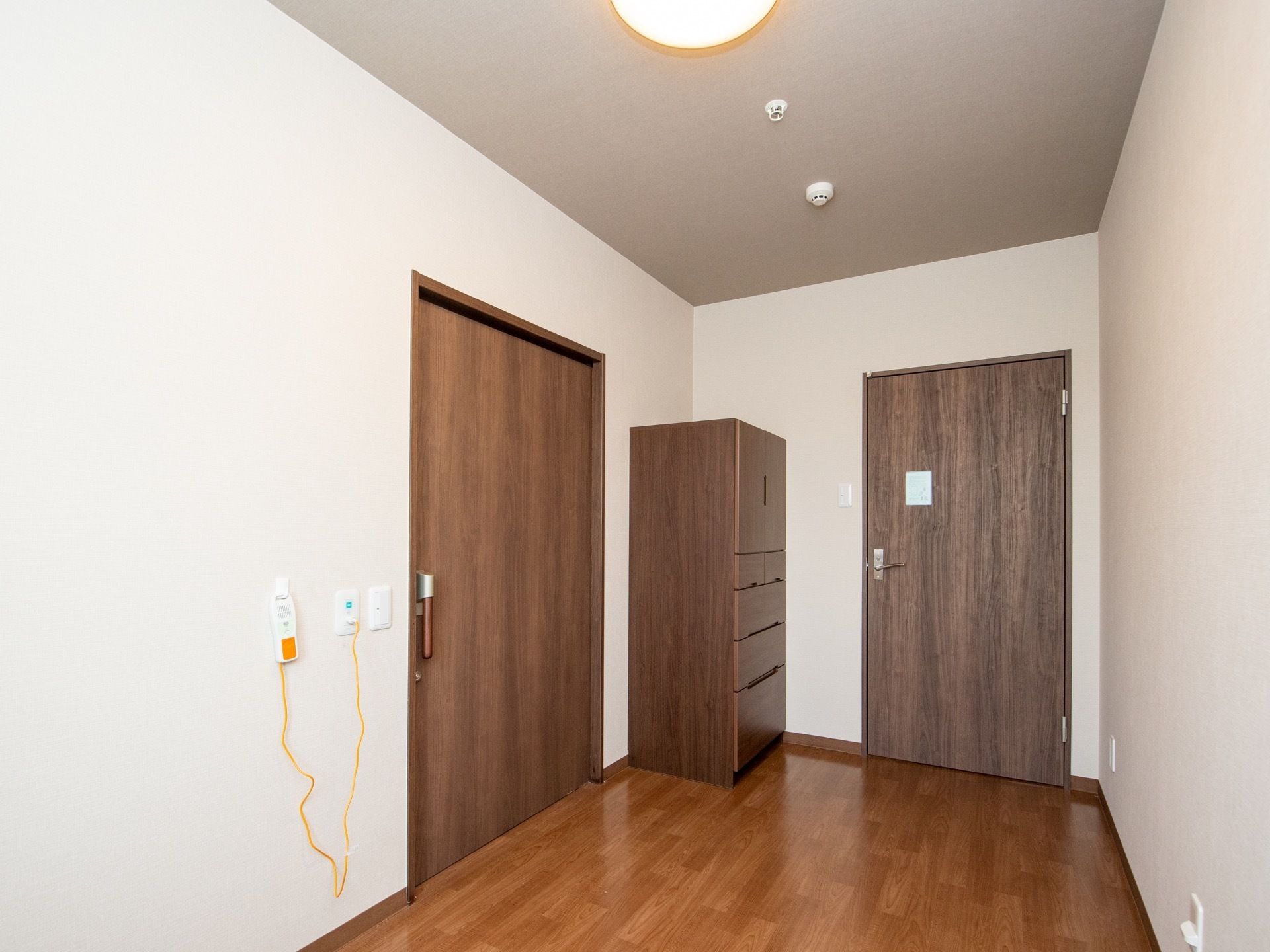 白い壁と、明るい茶色のフローリングの部屋である。焦げ茶色の扉が二つあり、部屋の角にタンスが一棹置かれている。