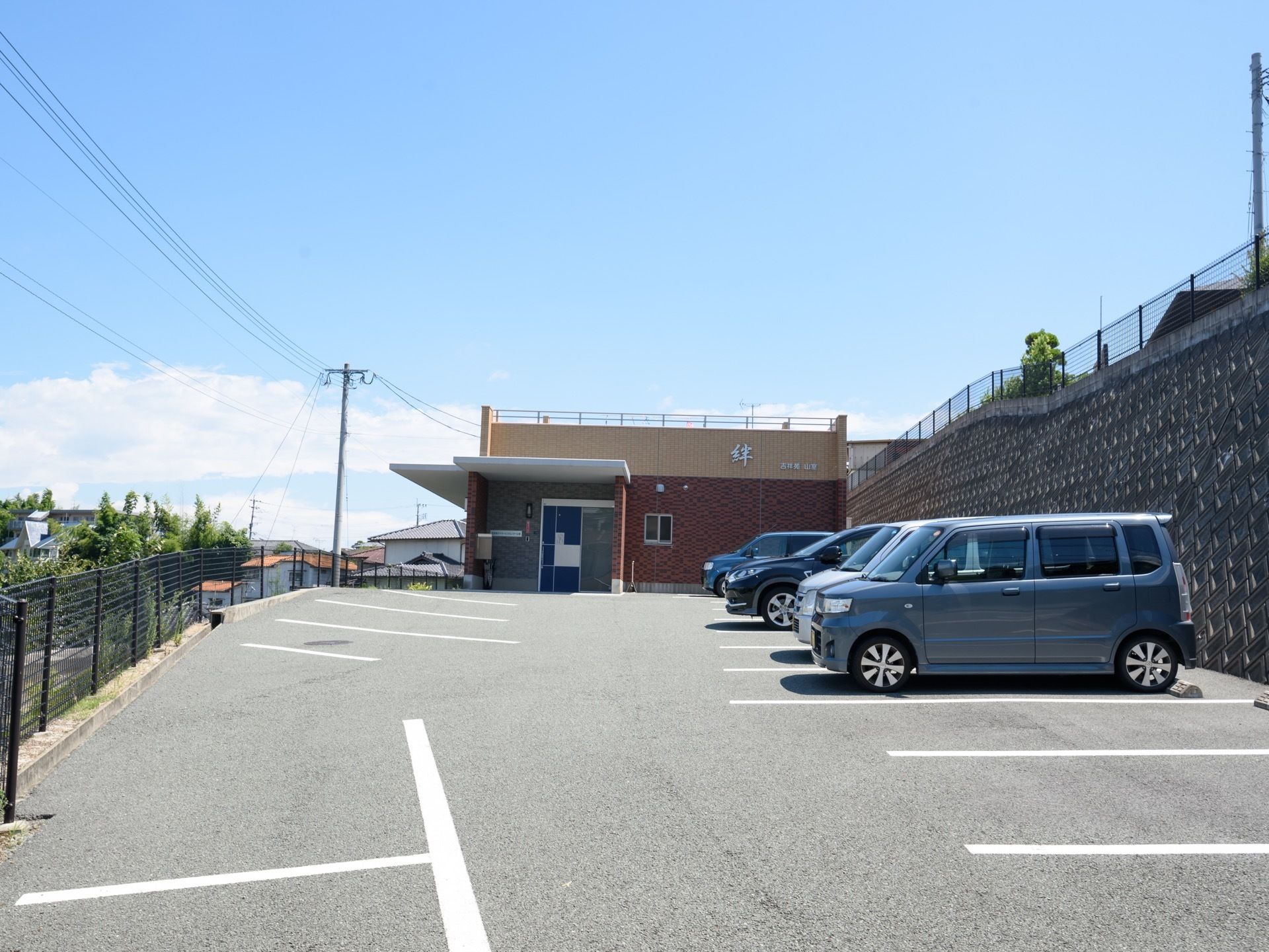 住宅街の中にあるグループホーム。坂の上に建っており、敷地内にはアスファルトで舗装された駐車場を完備している。