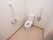 清潔感のある洋式トイレである。壁には手すりやナースコール、トイレットペーパーホルダーが設置されている。