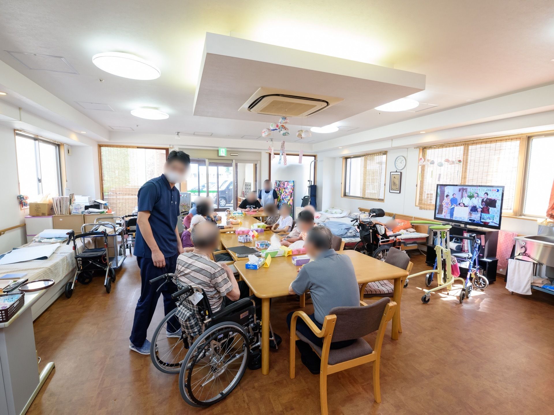 多くの入居者様が集まりテーブルを囲んでいる。エプロンを掛けたスタッフと一緒に小物作りを行っている入居者様もいる。