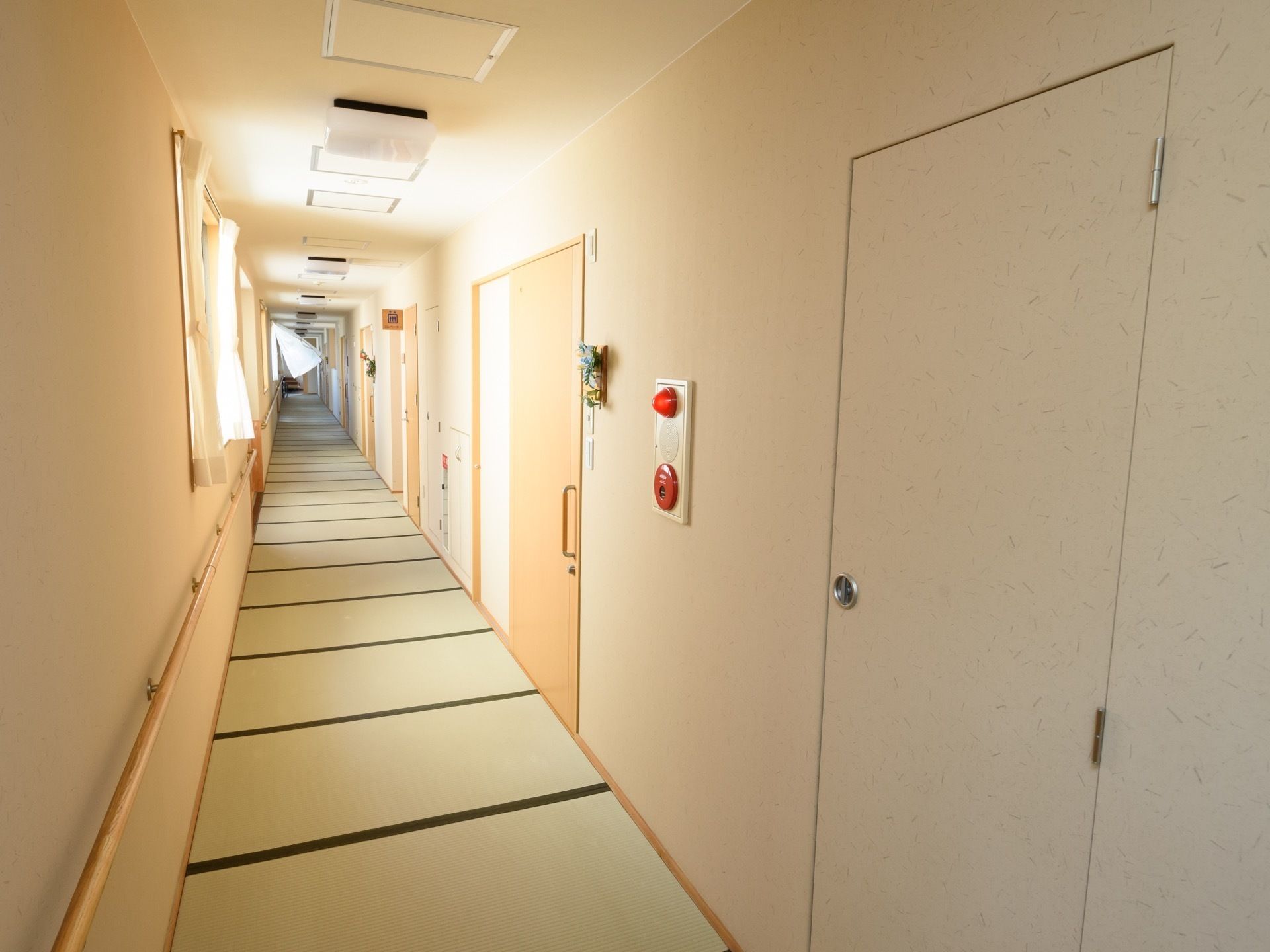 直線的な廊下で、床には畳が敷かれている。左側の壁には手すりが設置されており、右側には消火設備がある。