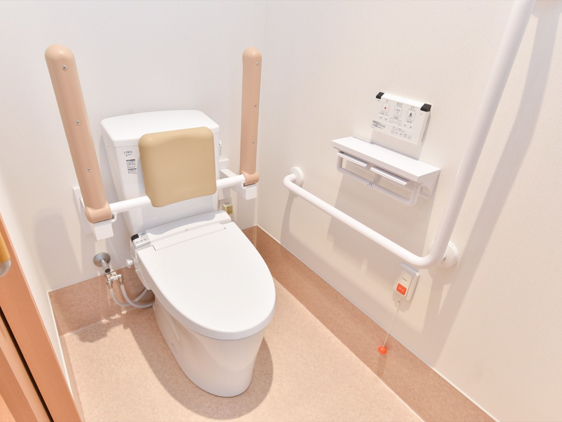 温水洗浄便座を完備したトイレは、手すりの他に折り畳み式のひじ掛けを用意している。背もたれのパットもある。