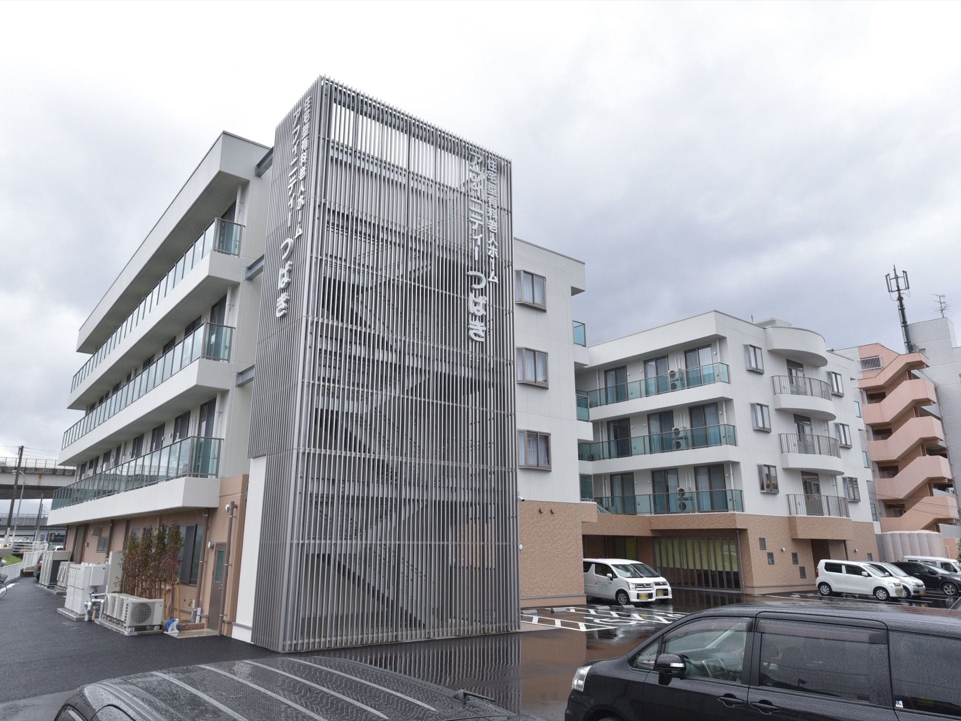 施設建物の外観。外に設けられた非常階段が金属製の箱のような大きな柵で覆われている、特徴的な外観をしている。