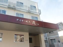 建物は３階建てで、２階と３階の窓の外には柵が設けられ、エアコンの室外機が置かれている。玄関の大きなひさしに施設名が表示されている。