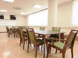 床はフローリングになっており、木製の長方形のテーブルを囲むようにグリーンの手すり付きの椅子が置かれている。室内には広い窓があり明るい。