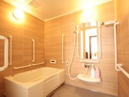 浴槽付近の壁には、縦型、横型の手すりが多数付いている。壁には鏡とシャワーが設置されている。壁の色は落ち着いた茶系で、照明設備が整っている。