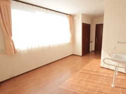 カーテンの掛かった広い窓から光が入り込んで明るい。広々とした床はフローリングになっている。右側に洗面台の両側に付けられた手すりが見える。