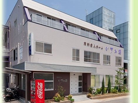 エントランス前に自動販売機が置かれ、壁に施設名の看板がある3階建の建物