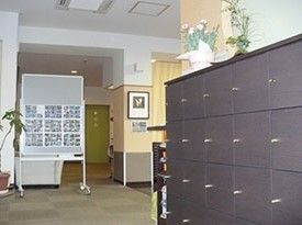 白を基調とした壁面に、一部ベージュの色合いの壁やカーテンが目を引く明るいエントランスである。靴箱や床面の各所には観葉植物が飾られている。