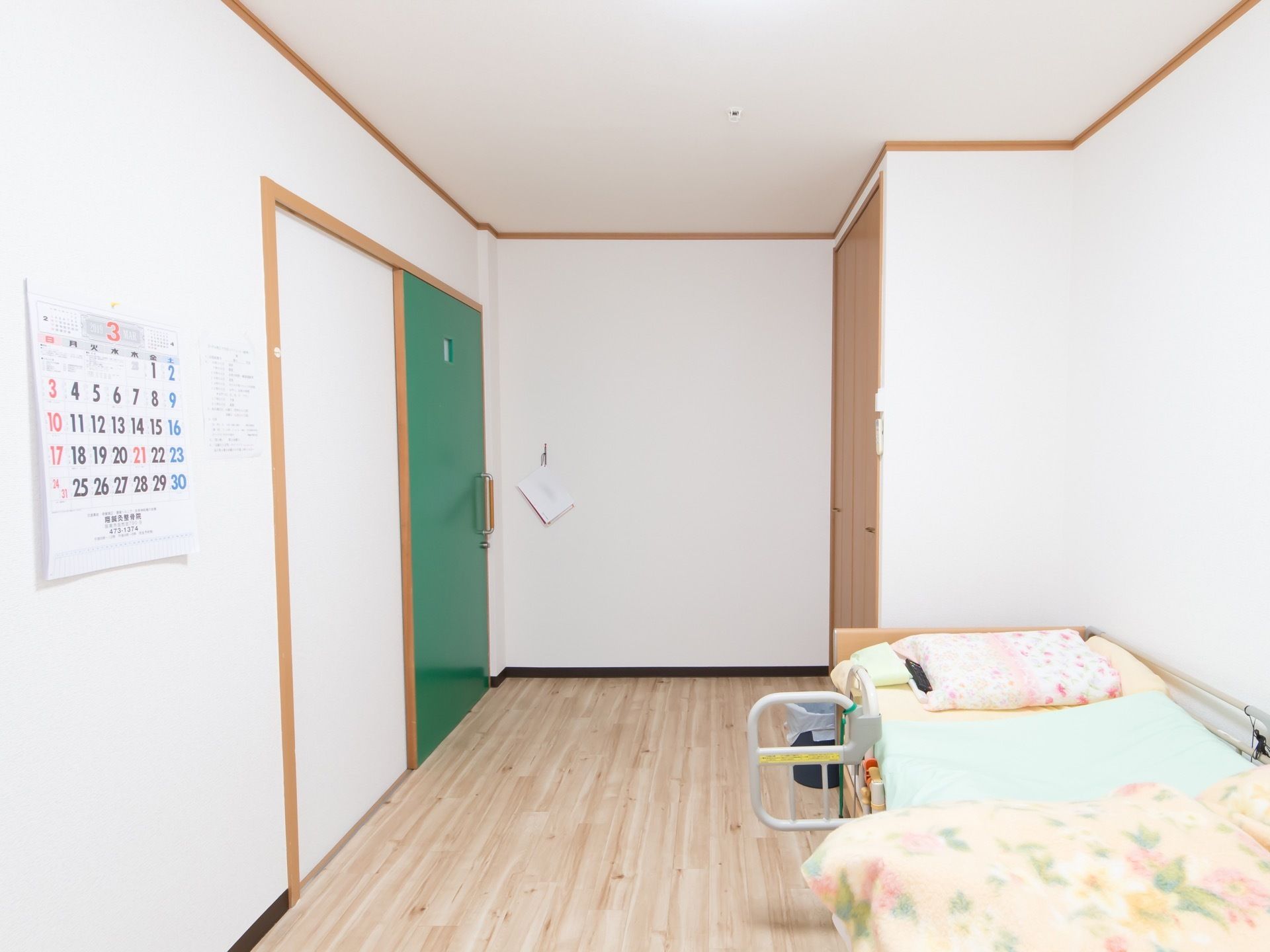 居室出入口は、鮮やかな緑色のスライドドアである。大きな数字でとても見やすいカレンダーが、左側の壁に貼ってある。