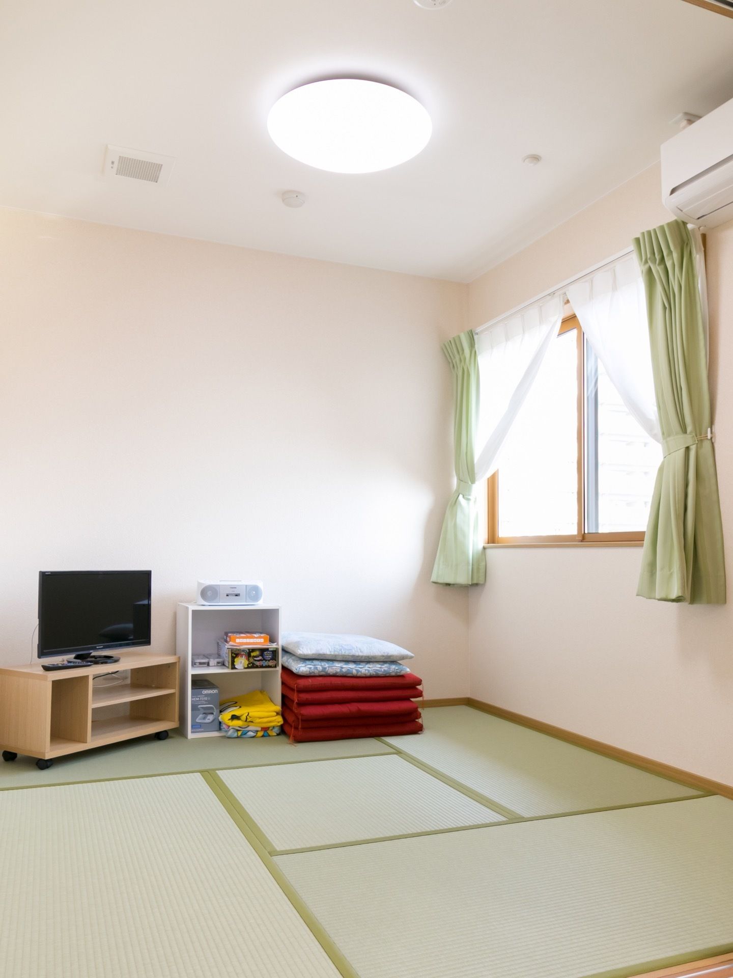 畳敷きの多目的室をリビング設けている。エアコンやテレビが設置されており、数枚の座布団が用意されている。