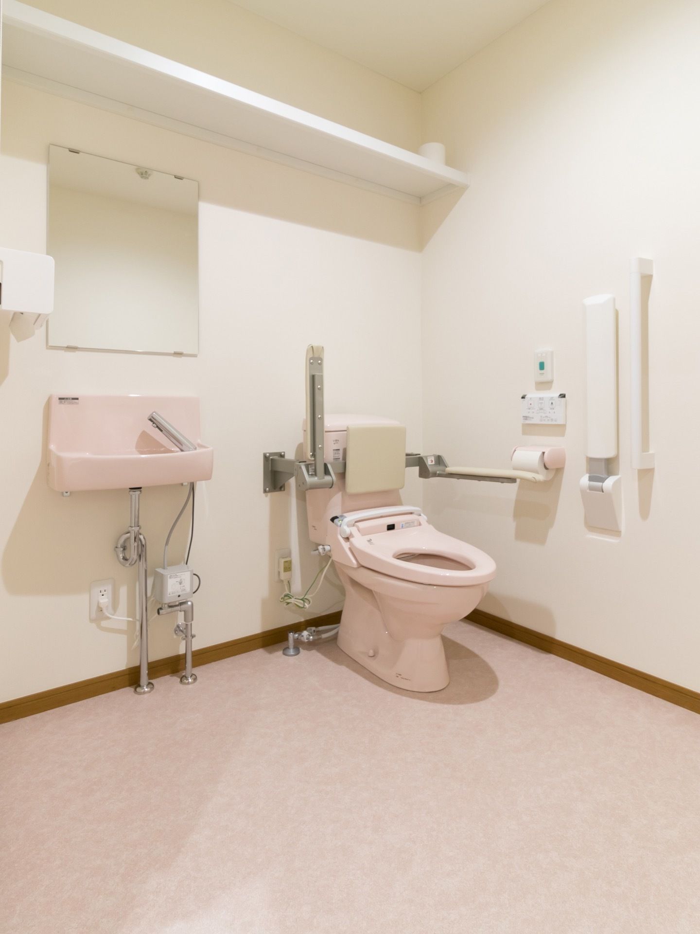 広々としたスペースのトイレである。Ｉ型手すりや可動式アームレストが設置されている。洗面台が備わっている。