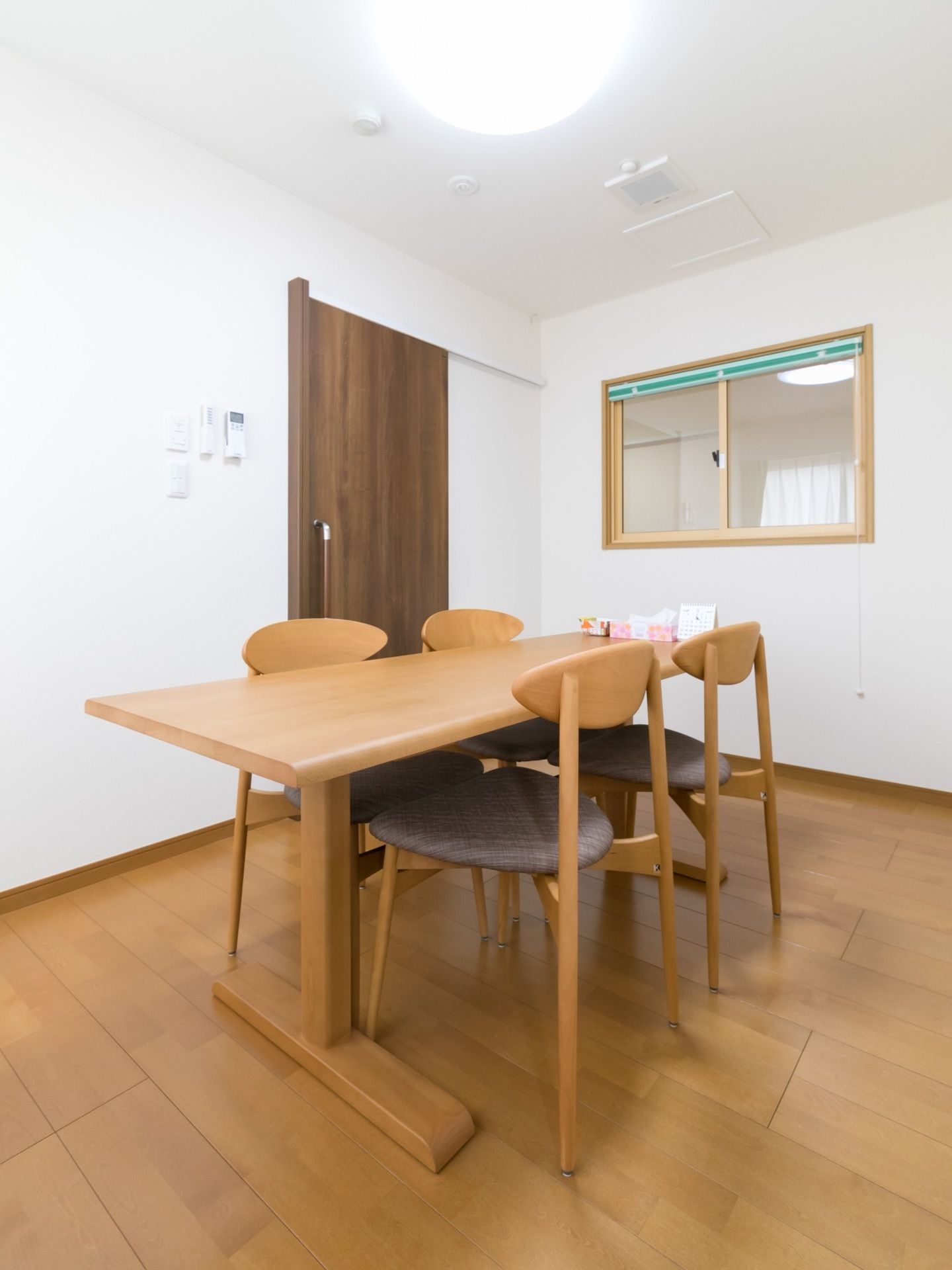 シンプルな相談室には、４人掛けテーブルが置かれている。壁には、電気のスイッチやエアコンのリモコンが設置されている。