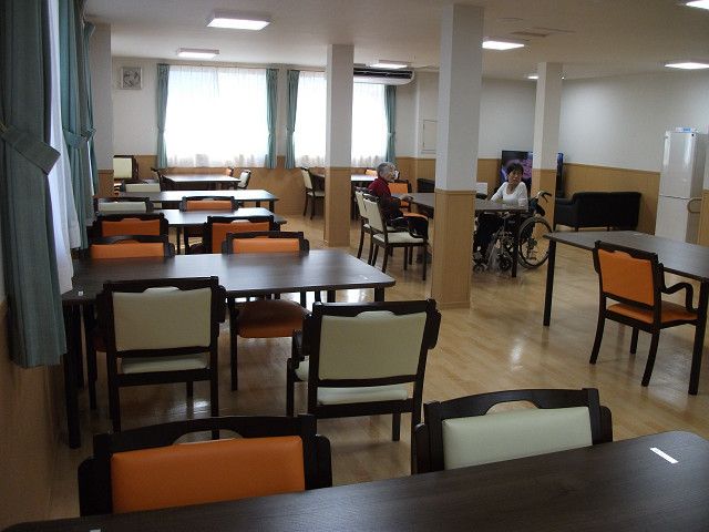 食堂の床はフローリングになっており、木調のテーブル、手すり付きの椅子が置かれている。窓から光が差し込み、室内は明るい。