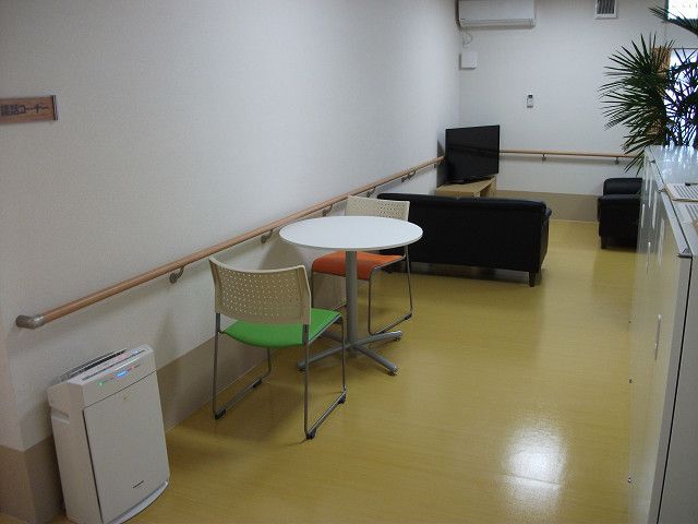談話スペースには、テレビ、ソファ、テーブル、椅子が置かれているほか、壁には手すりが設置され、観葉植物、空気清浄機も置かれている。