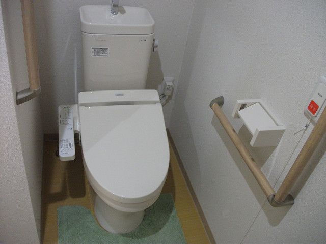 トイレには温水洗浄便座が置いてあり、便座の両側に手すりが設置され、緊急呼び出しボタンも付いている。壁の色は明るいベージュ系である。