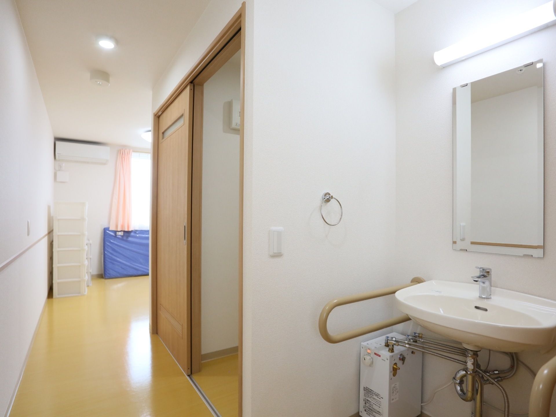 居室には、両側に手すりが設置された洗面台がある。専用の照明や鏡があり、便利である。フローリングや壁の色は明るい色が使われている。