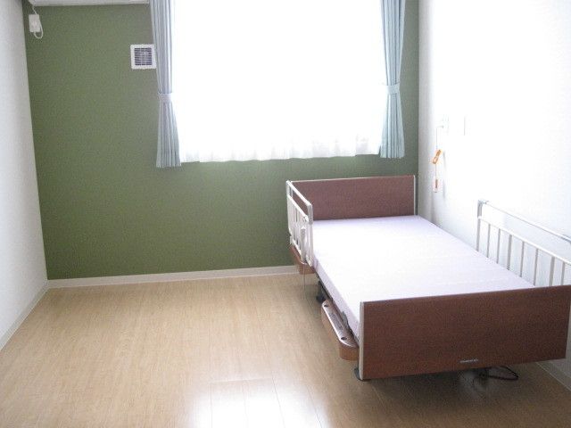 居室にはエアコン1台、ベッド1台が用意されており、ベッドには転倒防止の手すりが付けられている。呼び出しボタンもある。