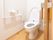 木目調のフローリング材を使用した、明るい雰囲気のトイレである。洋式便座を完備。壁にはトイレットペーパーホルダーなどがある。