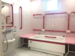 ピンク色の介助テーブルに赤の手すりというオシャレなデザインの浴室ではお１人ずつ入浴を楽しんでいただくことができる。
