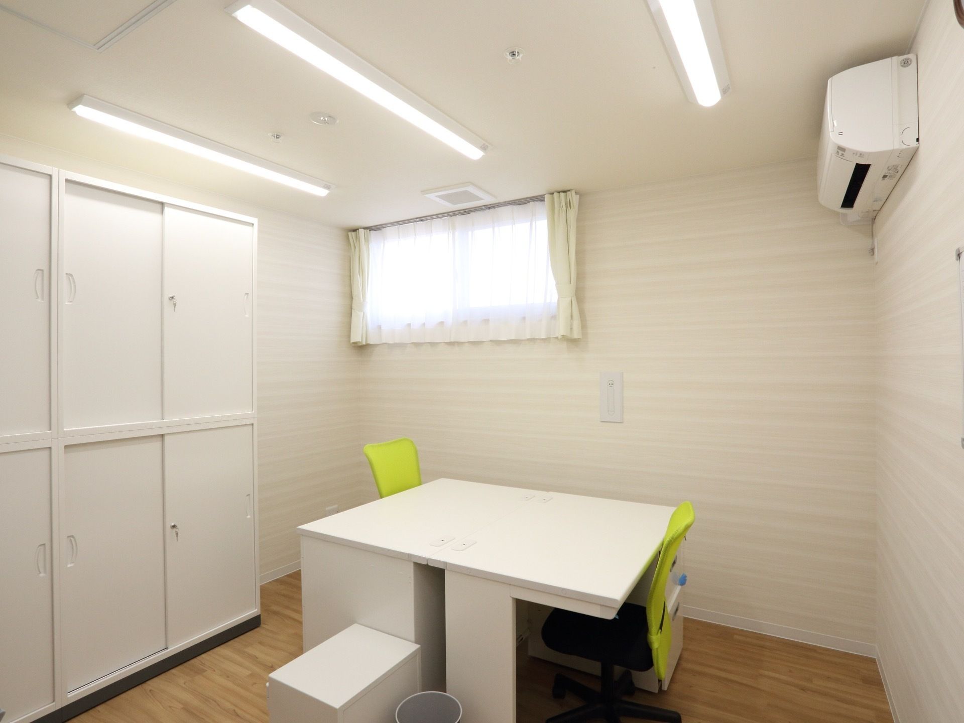 白を基調とした部屋にテーブルや椅子が置かれている。小窓が設置されていて、収納棚も置かれている。黄色い蛍光色の椅子が目立っている。