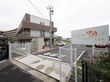建物の傍らに広い駐車場がある。フェンスで囲まれ、舗装されている。入口付近には施設の名前が書かれた大きな看板が設置されている。