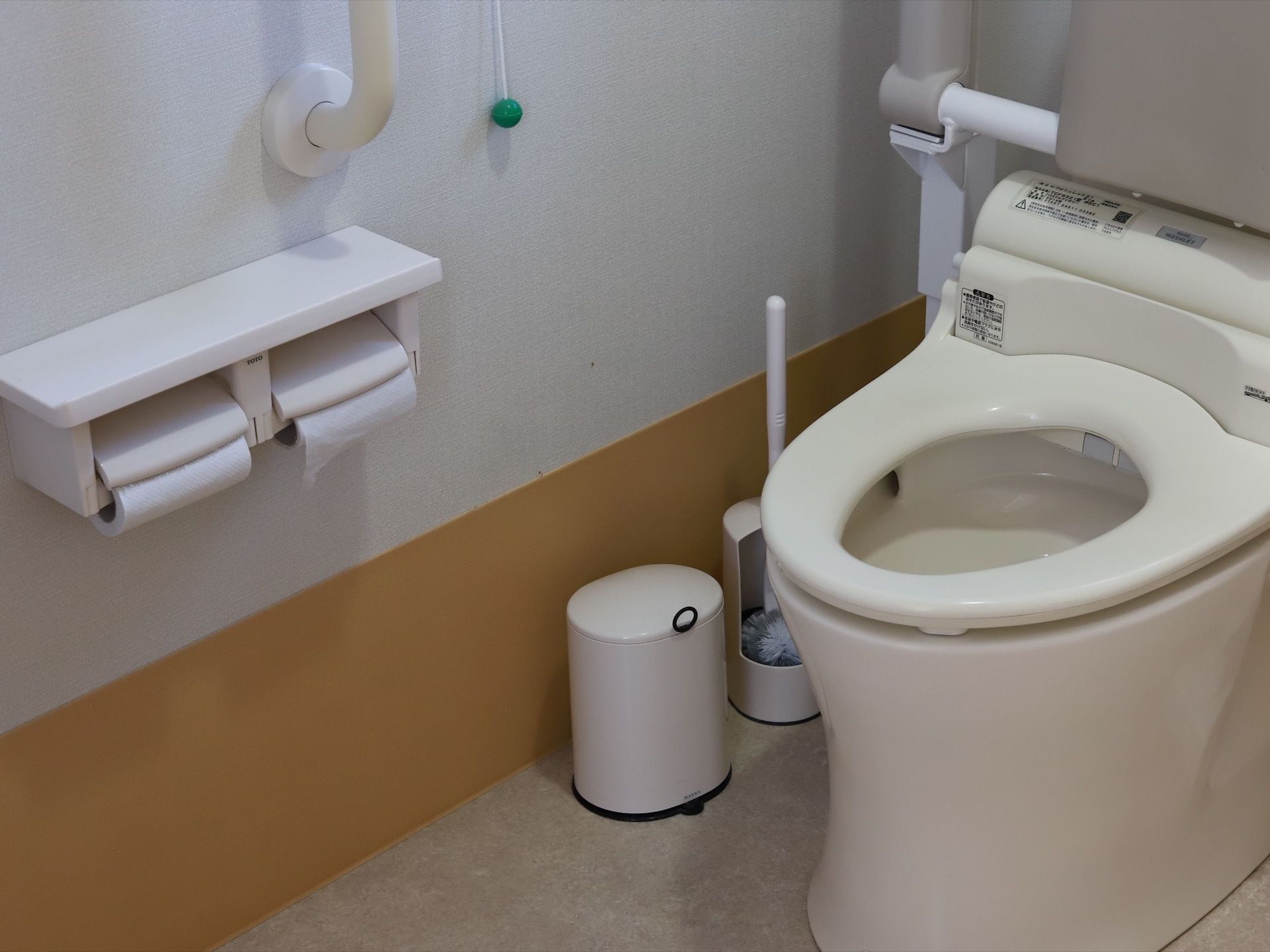 清潔感があるトイレになっている。手すりを壁に設置しており、安全に利用することができる。床には清掃用のブラシが置いてある。