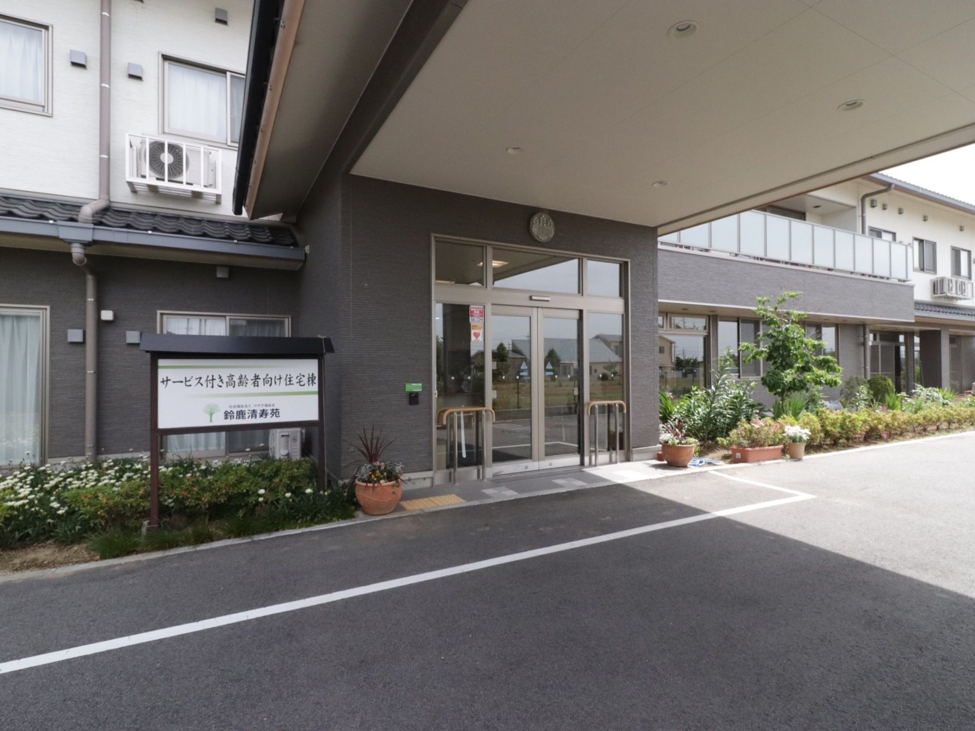 広い敷地に立地している施設の外観。ダークグレーを基調とした落ち着いた雰囲気になっている。玄関前には屋根が設置されている。