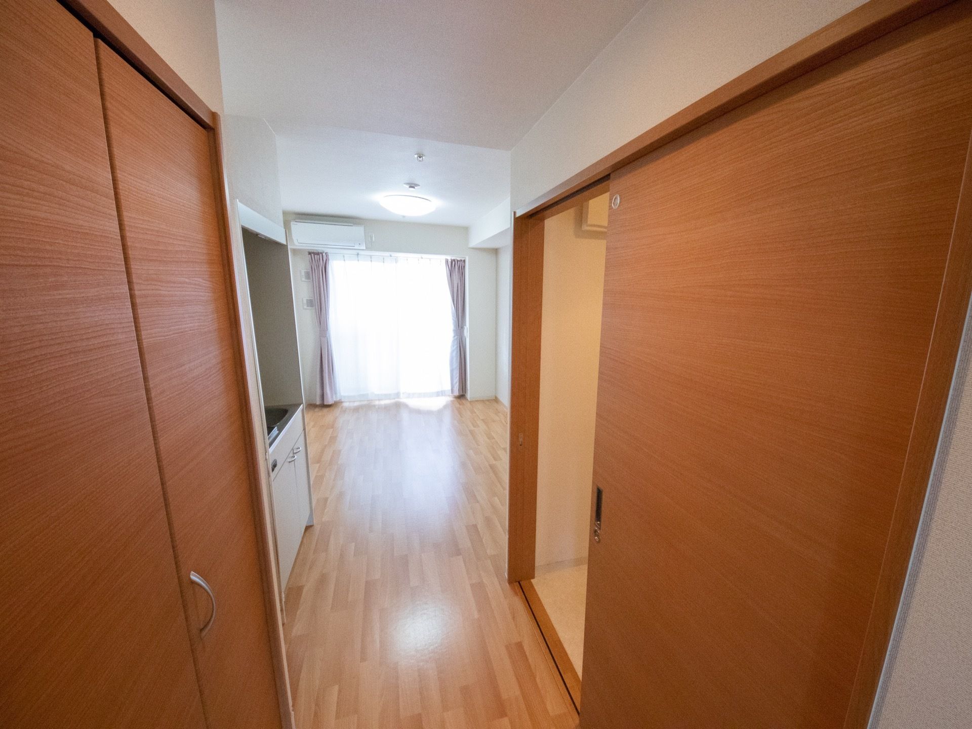 白色の壁と木目調のフローリングの床のシンプルな居室。部屋を入ってすぐ横には、トイレとクローゼットがある。
