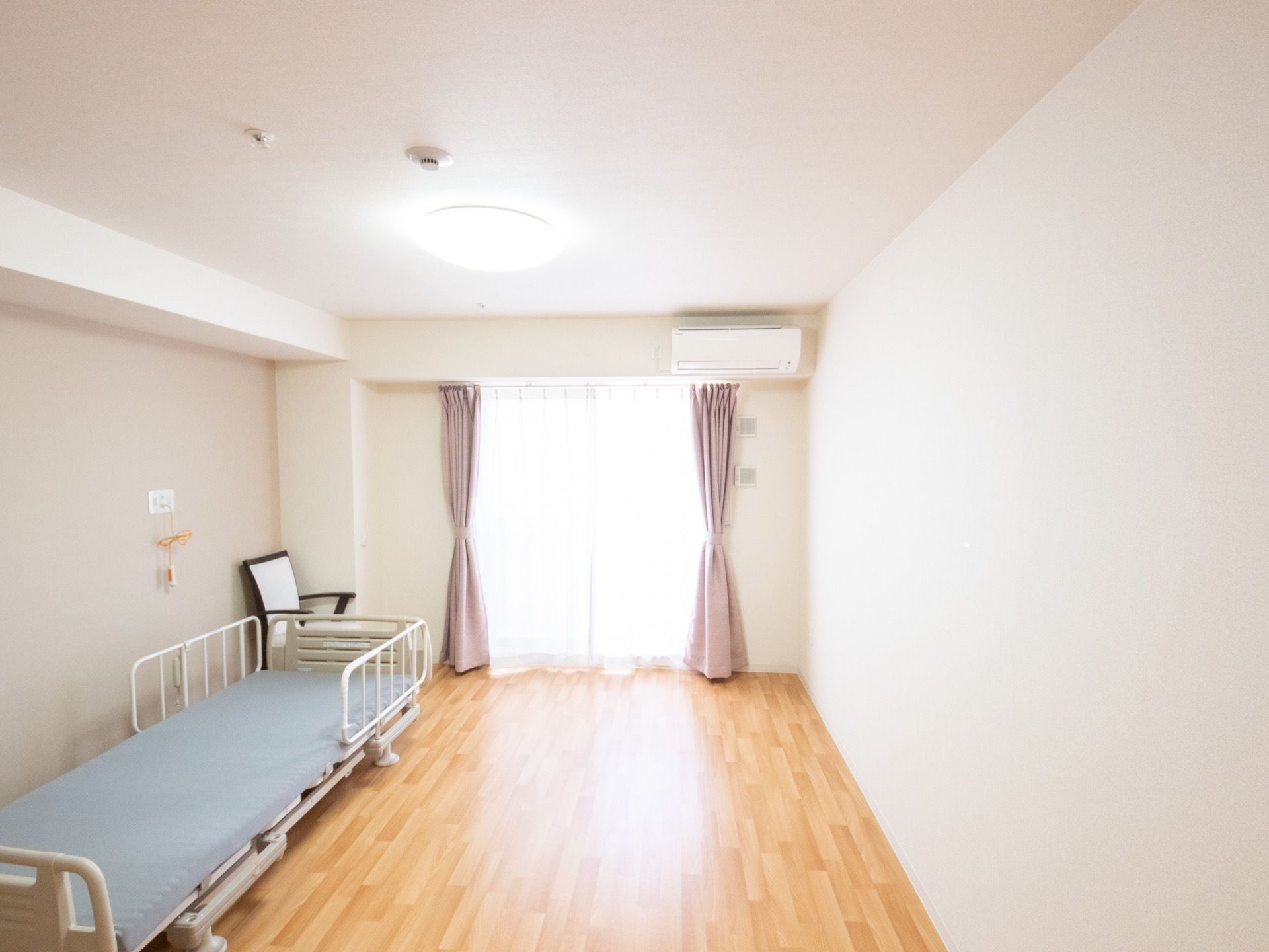 長方形のシンプルな部屋である。天井にはスプリンクラーと丸い照明が取り付けられている。窓の横には給気口が設置されている。