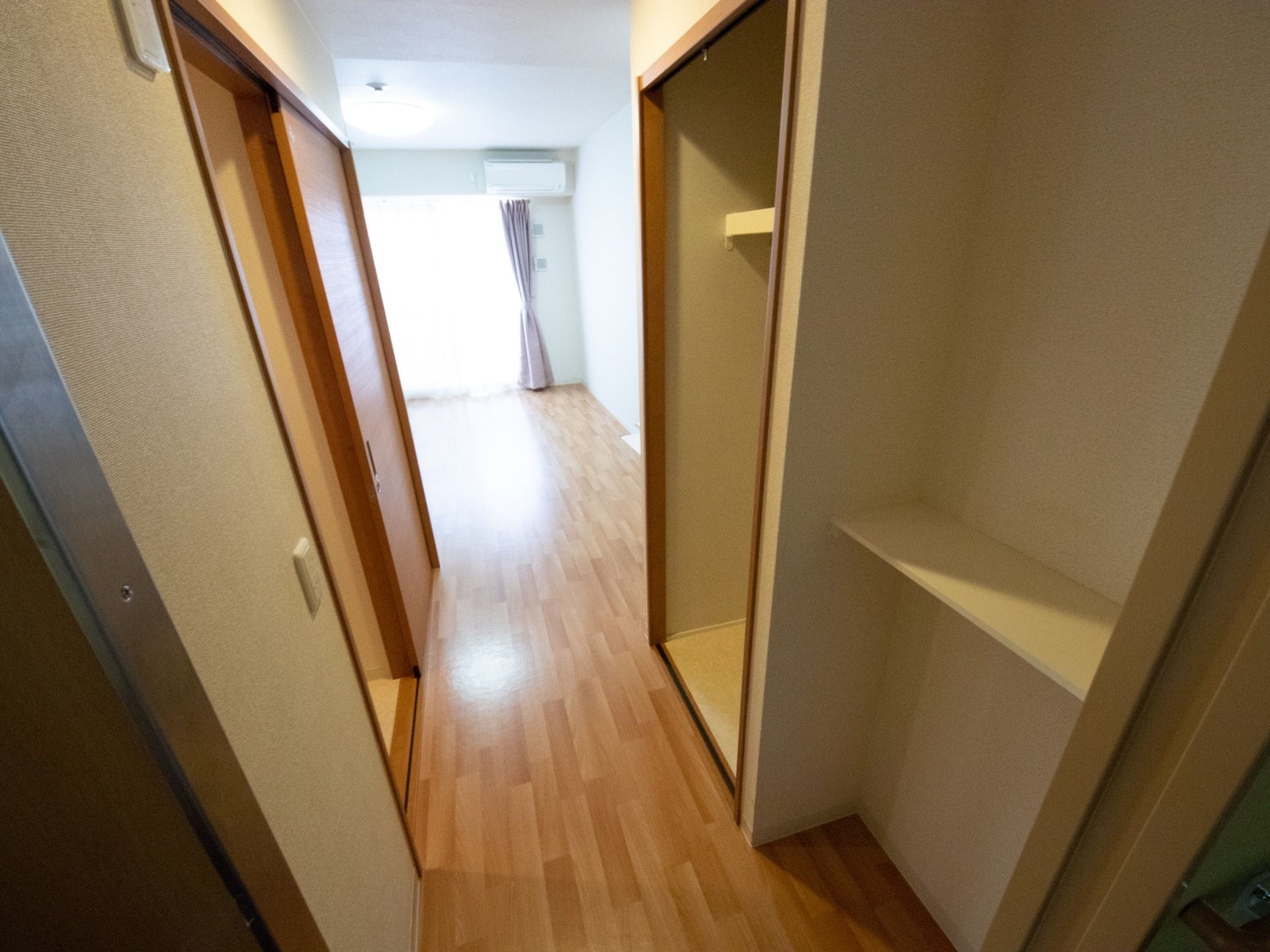 部屋を入ってすぐのクローゼット横に、白い板で作られた収納棚が取り付けられている。反対側には部屋の照明のスイッチが設置されている。