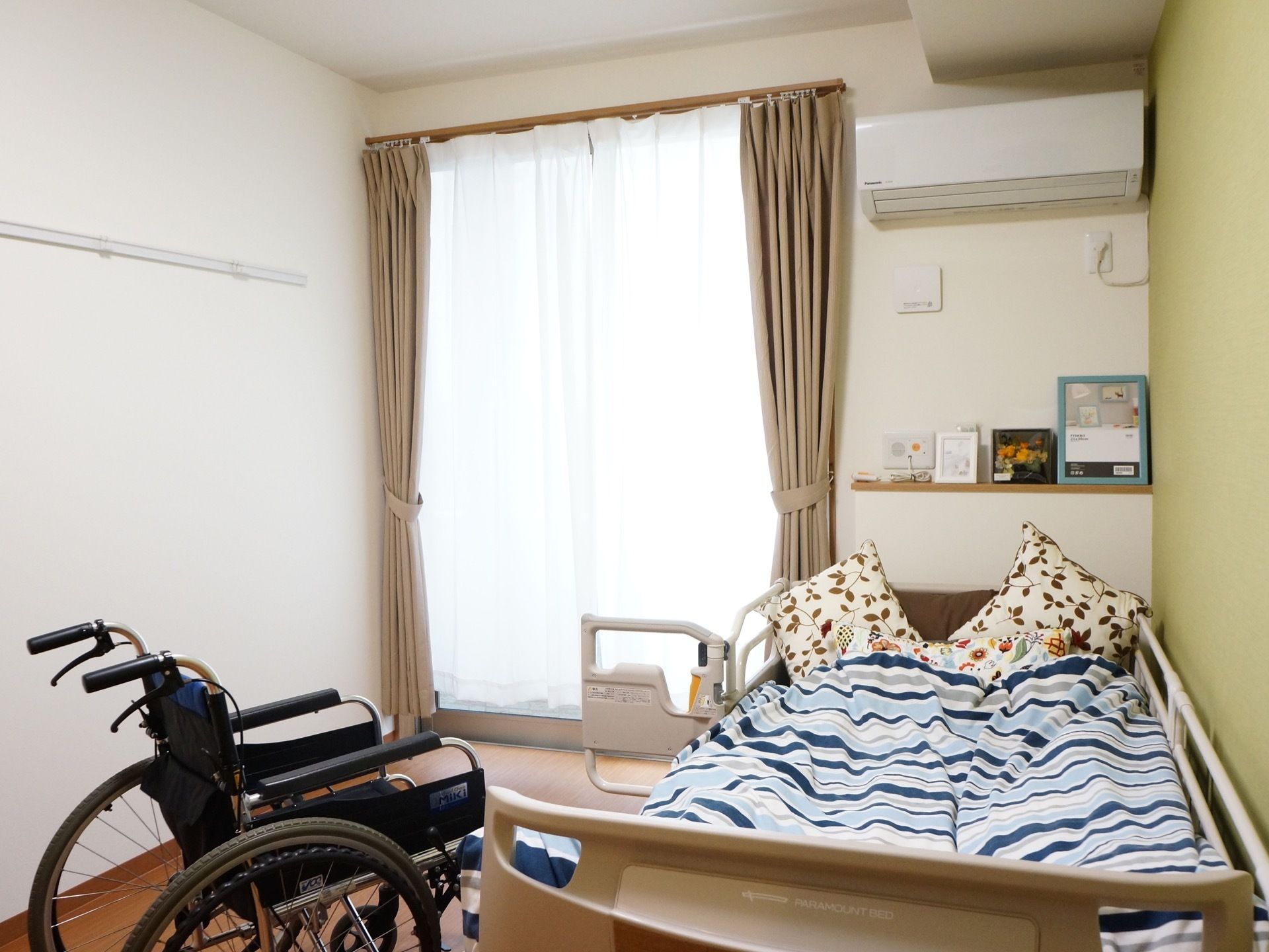 掃出し窓のある明るい居室である。窓際の壁には木肌色の棚が設置されており、カレンダーや写真などを飾ることができる。