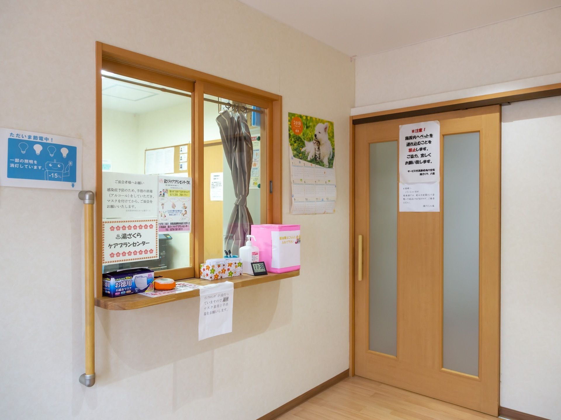 事務所の窓口はガラス張りなので、内からも外からも様子がうかがいやすい。さまざまな案内が貼られている。ご意見箱と消毒液が置かれている。