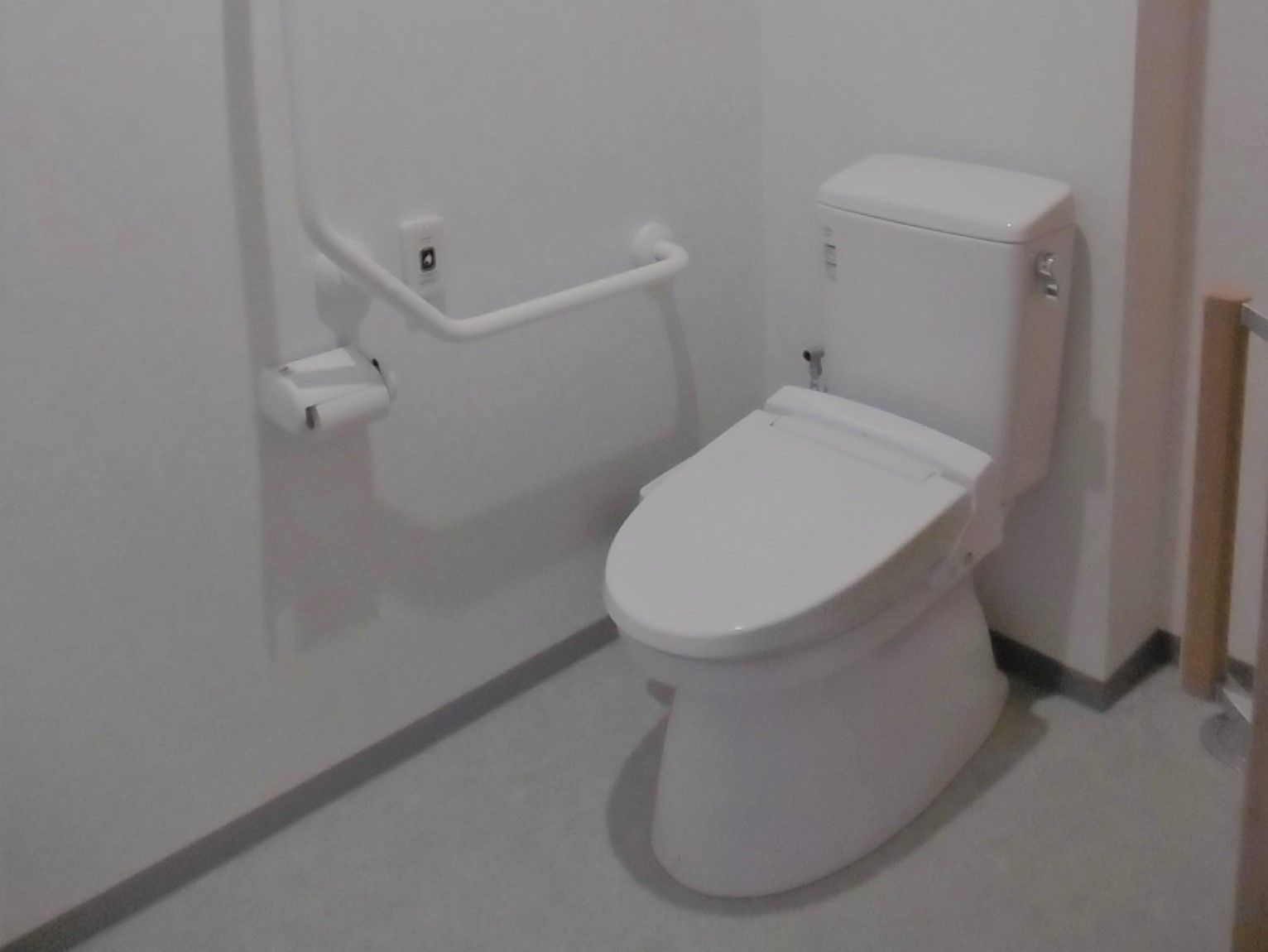 白基調の明るいトイレである。頭上や足元などスペースが広々としており、手すりも取り付けられている。安心して使用できる。