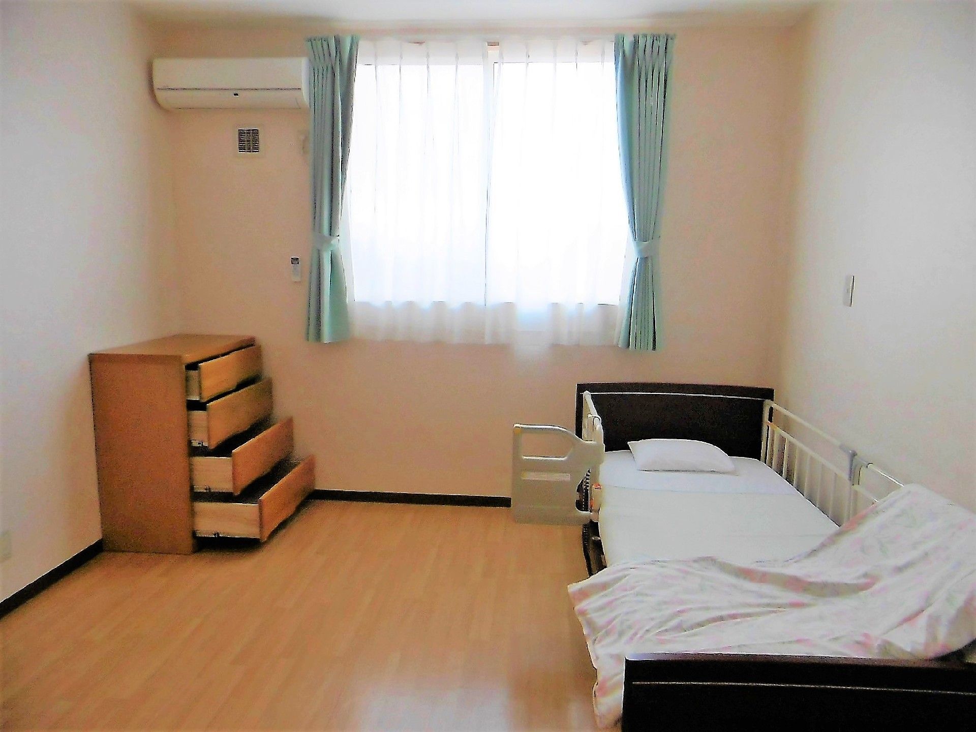 明るい色使いがされたお部屋である。大きな窓から光が十分に入り、ベッド外周部のバーで安全も確保されている。