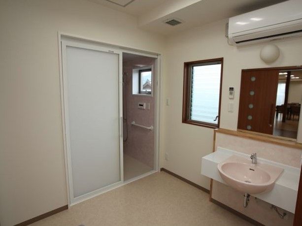 大きな鏡のある洗面台。上にはエアコンがついている。引き戸の奥には浴室があり、バリアフリーでつながっている。