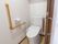 トイレは、全面が白色で統一された清潔感のある室内である。ドアはスライド式の引き戸で、壁には手すりが付けられている。