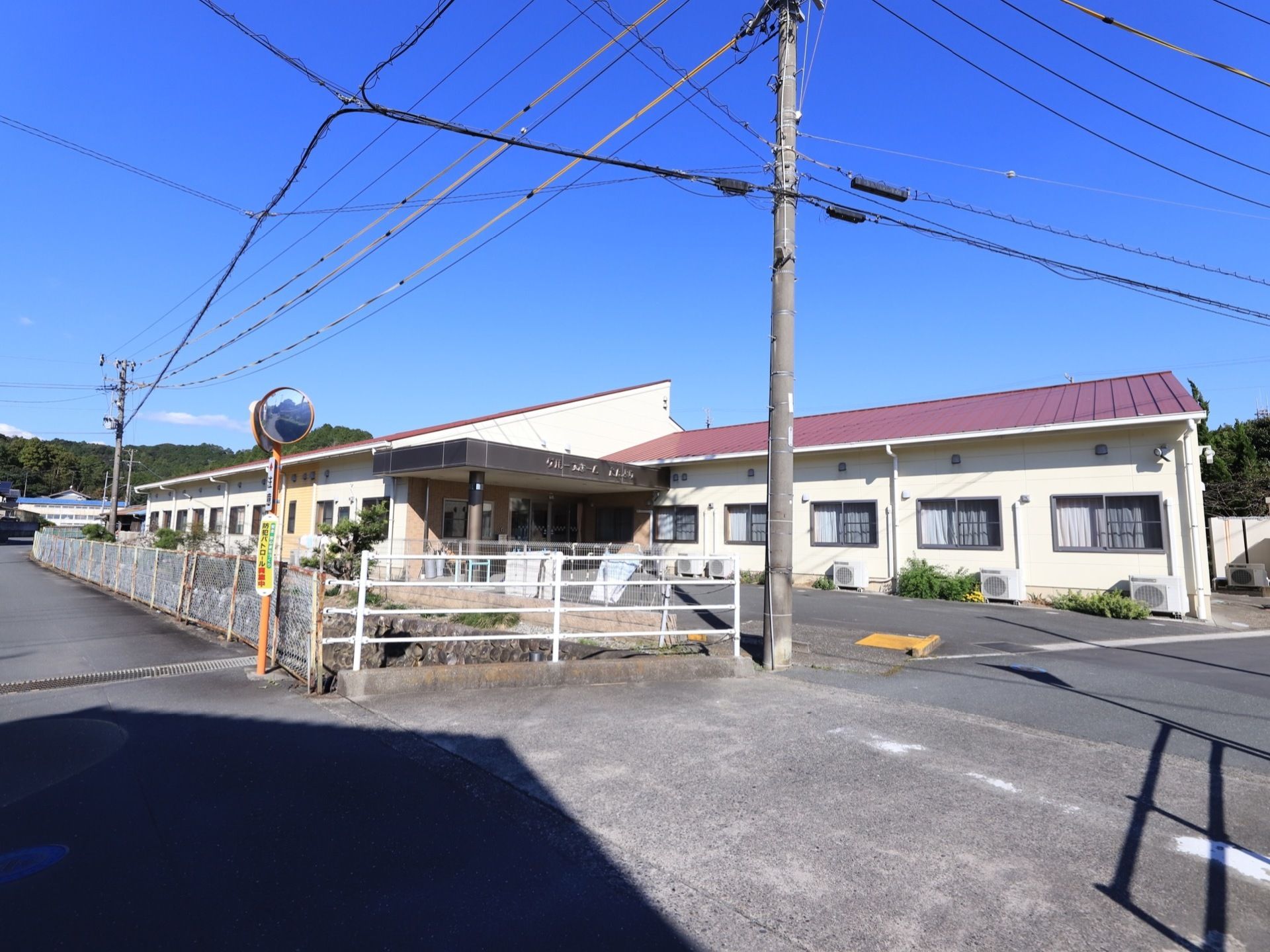 施設は赤色の屋根で、横に長い平屋となっている。玄関前には屋根のあるスペースがあり、駐車場も設けられている。
