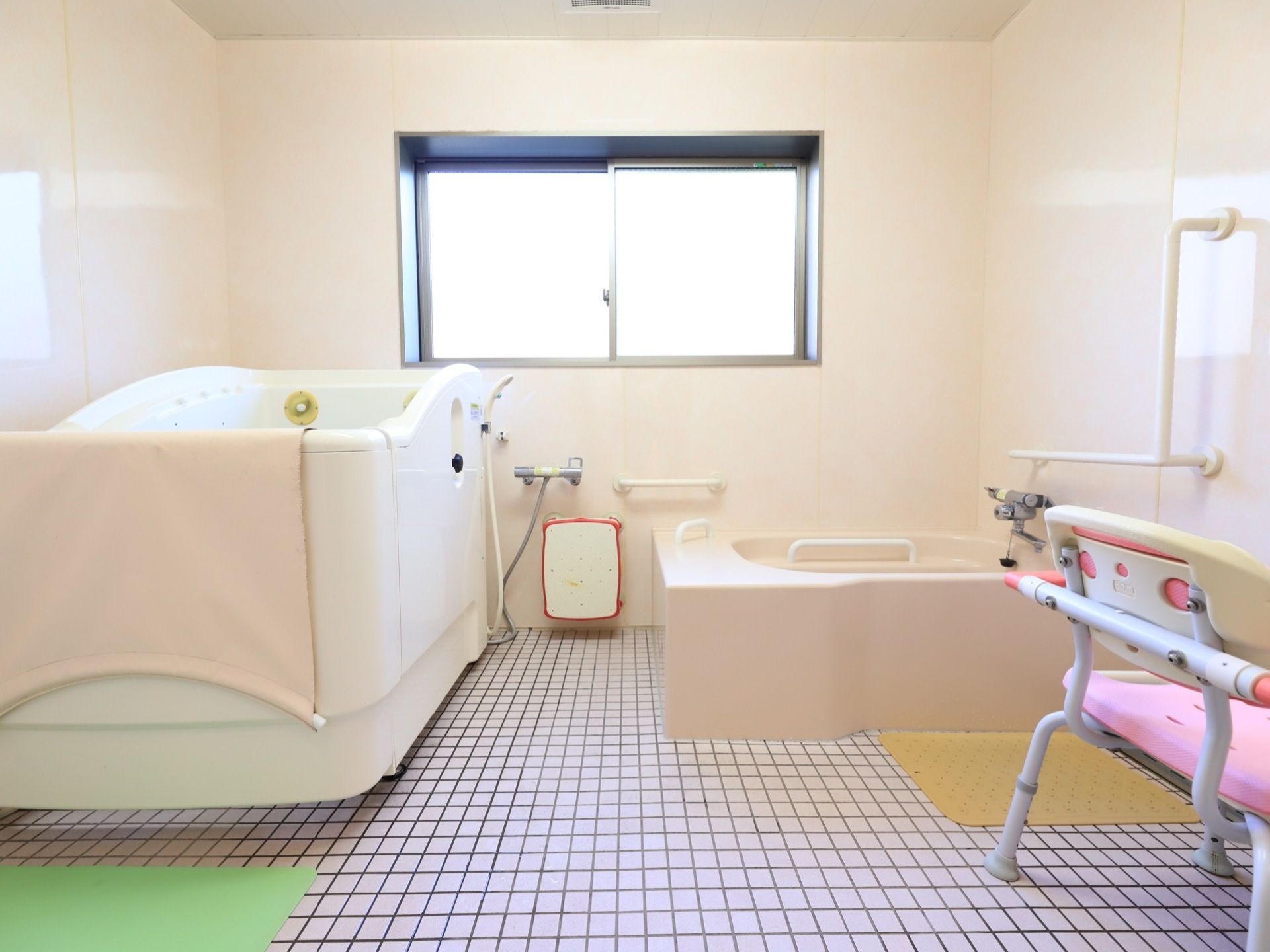 広々とした浴室には、介護用の浴槽と普通の浴槽が設置されている。床はタイル張りで、壁には手すりが取りつけられている。