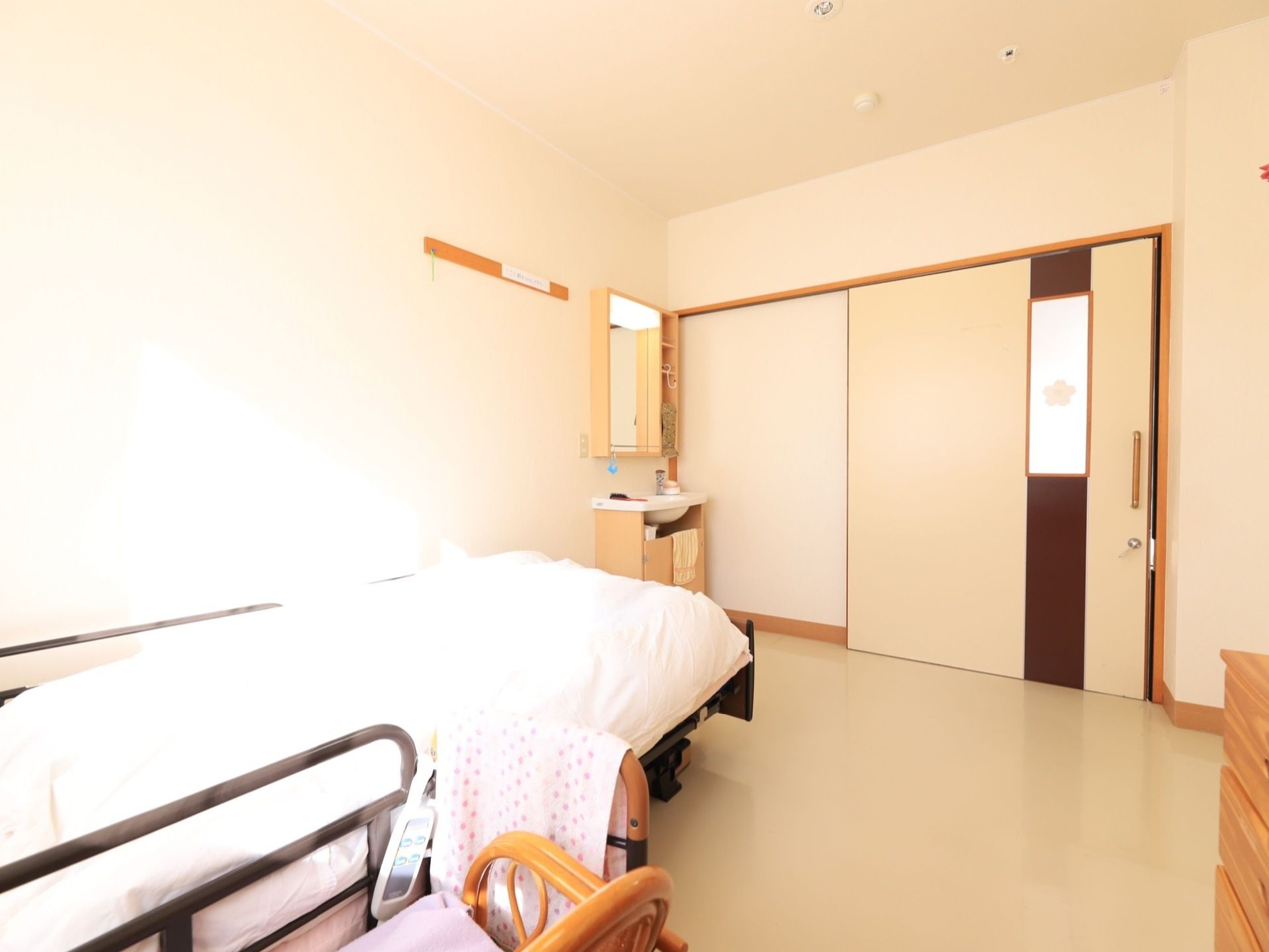 入居者様の居室には、シングルベッドが用意されている。部屋の隅に洗面台も設置されており、入口は引戸が取りつけられている。