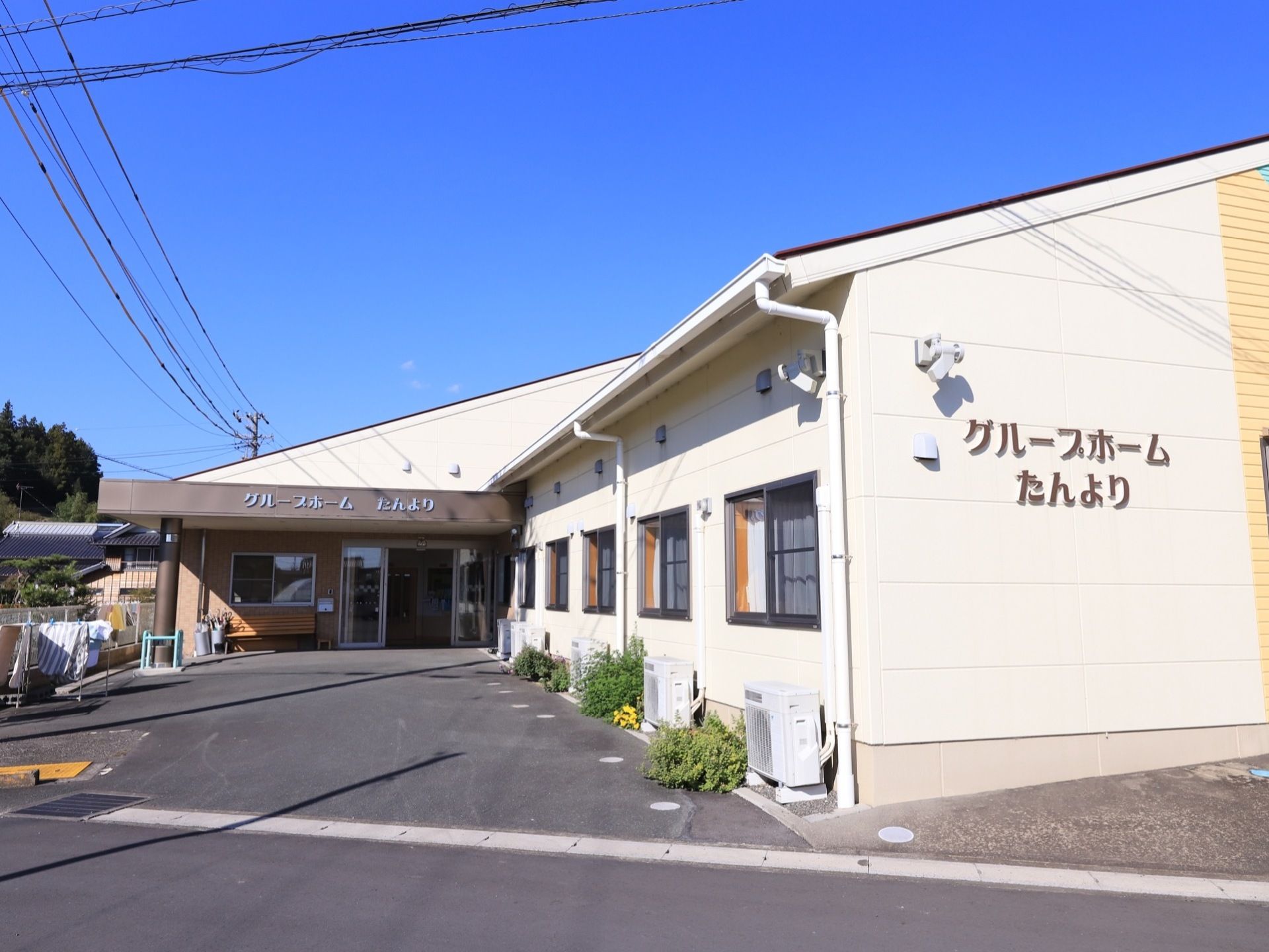 施設は一階建ての建物で、玄関に自動ドアが設置されている。そばにはベンチがあり、入居者様の居室の外にはエアコンの室外機が置かれている。