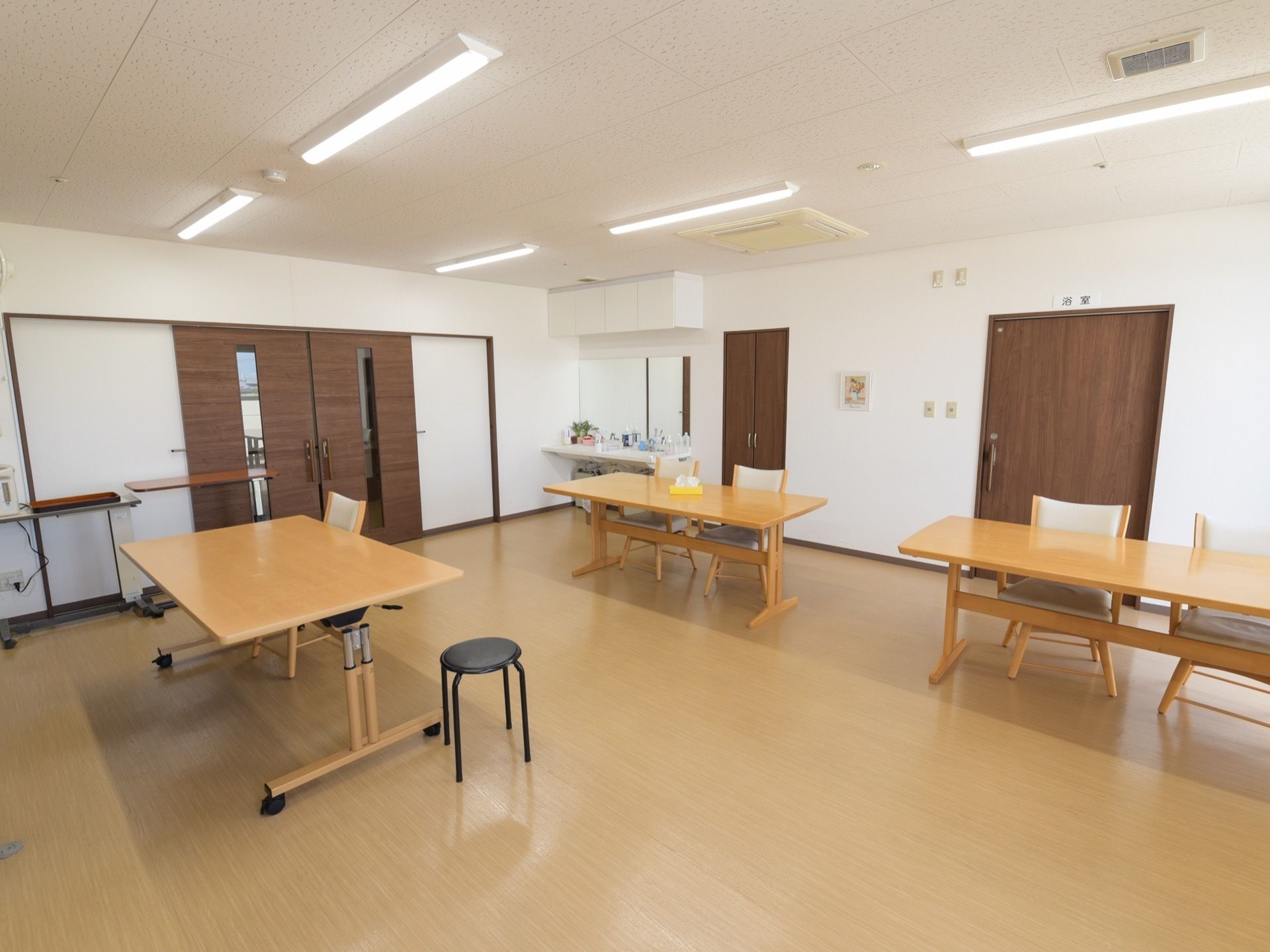 広いスペースにテーブルが3台、椅子が5脚と丸椅子が1脚ある。部屋の入り口は引き戸式のドアである。空調設備が完備されている。