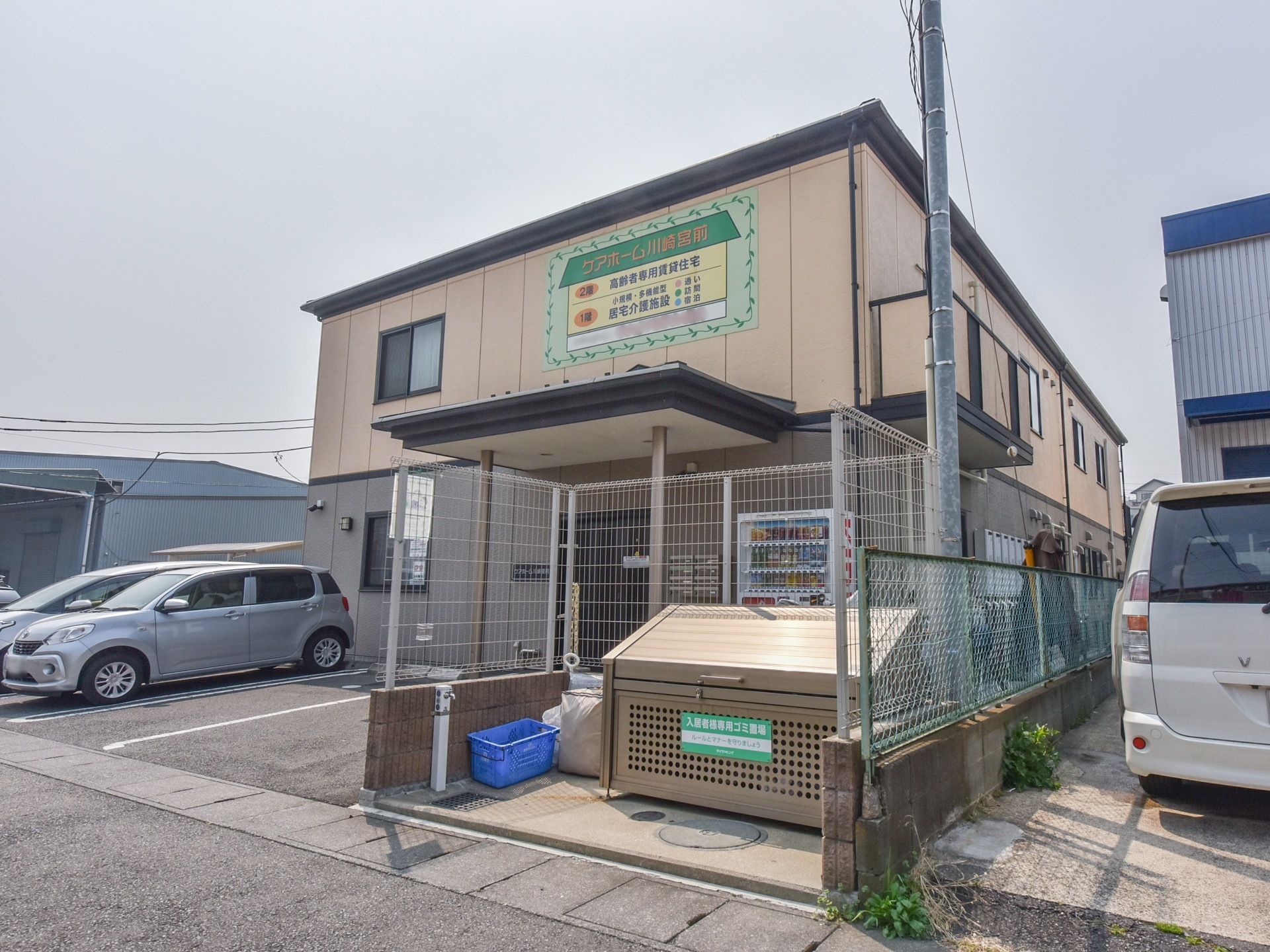 建物外壁に大きく施設名の書かれた看板が貼られている。入口横に自動販売機が置かれている。施設の前は駐車スペースとなっている。