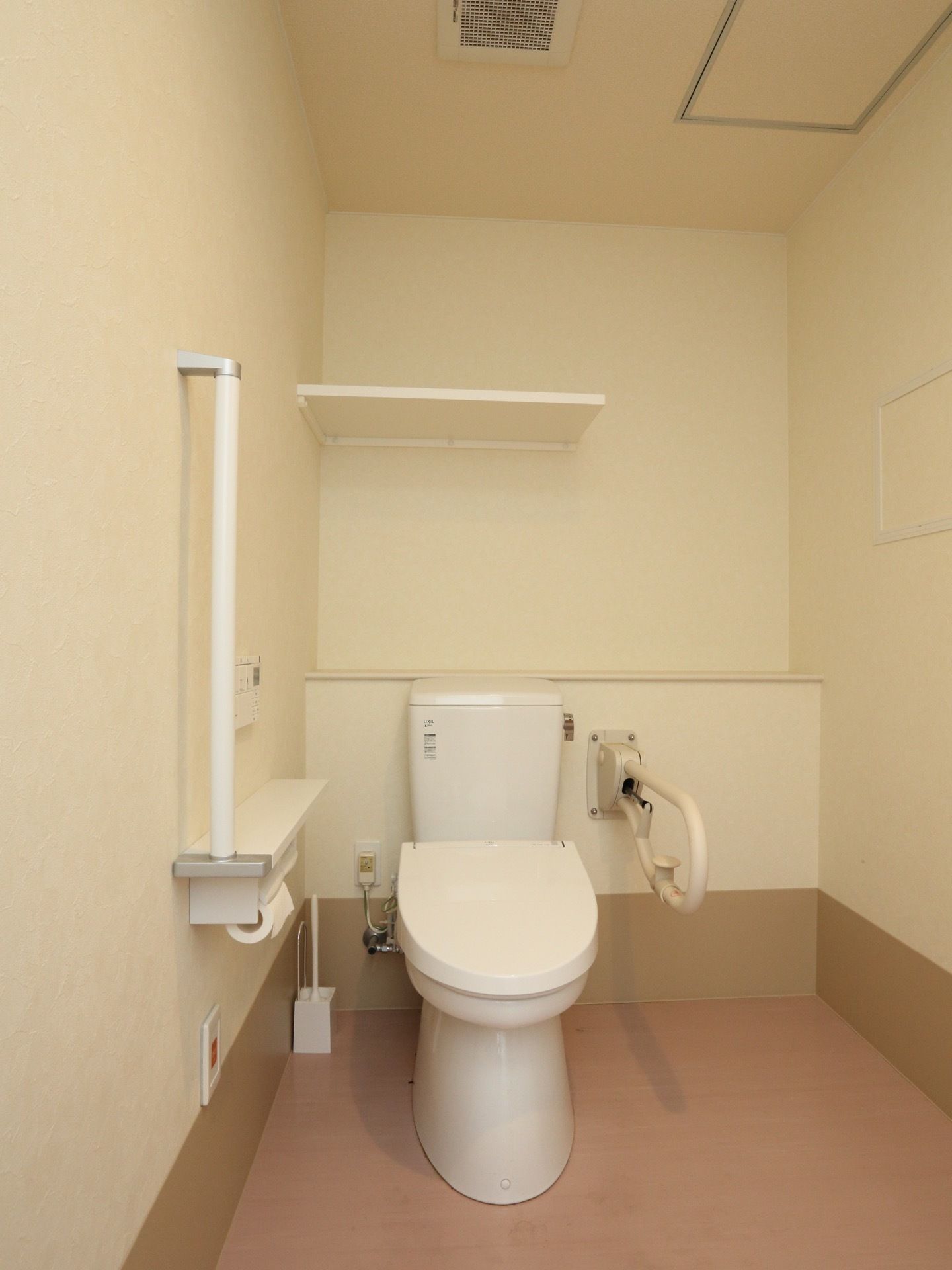 トイレの左側の壁にはペーパーホルダーがあり、その上に細長い棚とＩ字型の手すりがついている。奥には収納スペースもある。