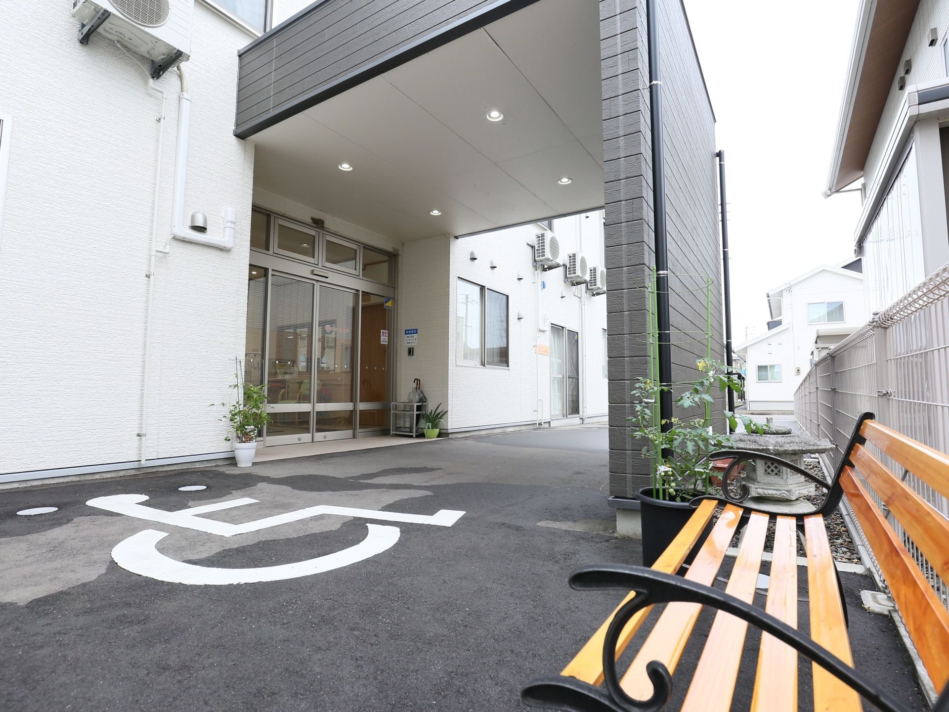 屋根付きの広々とした車寄せスペースのある玄関。大きな自動ドアがあり、脇には傘立てや観葉植物が置かれている。
