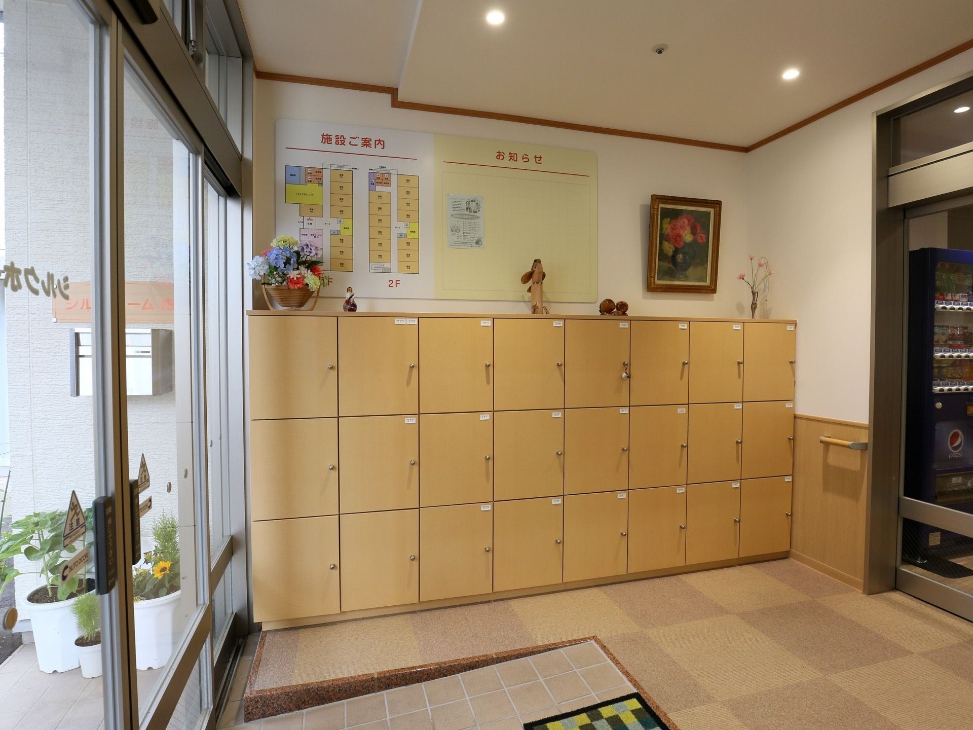 自動ドアを入ると緩やかなスロープになっていて、横に下駄箱が設置されている。下駄箱の上には施設案内の看板がついている。