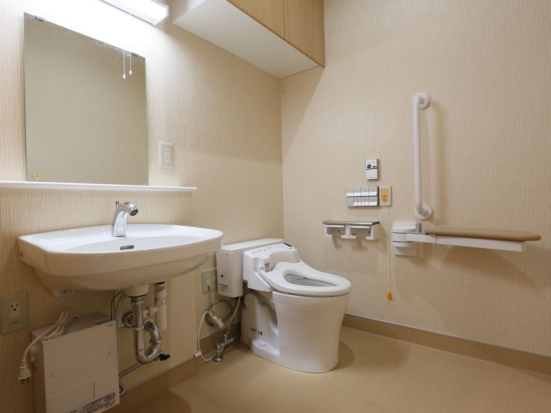 車椅子対応の広いトイレがある。便座の横には手すりが設置されていて、手すりの脇には緊急通報装置も付けられている。
