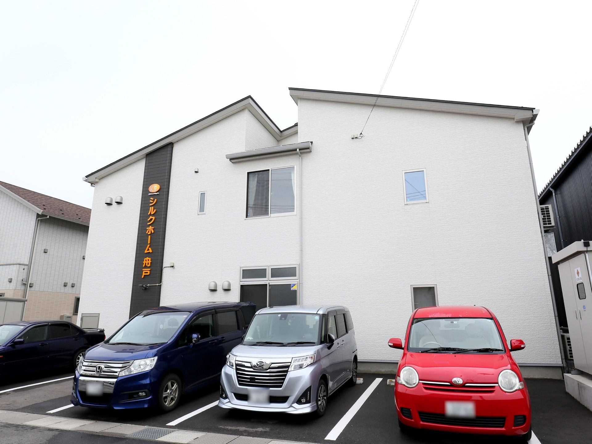 2階建ての建物があり、目の前は駐車場になっている。建物の外壁は白く、黒い縦のライン上にホーム名が書かれている。